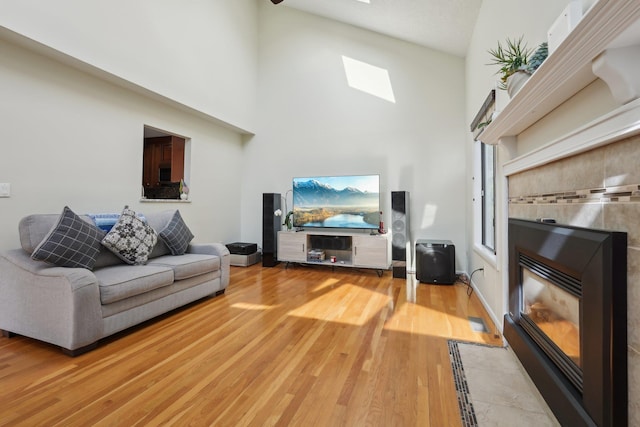 living area with a skylight, a tiled fireplace, wood finished floors, and a towering ceiling