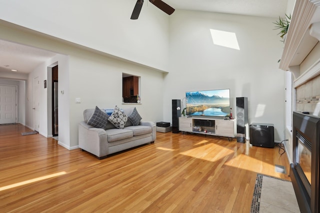 living room with a ceiling fan, a skylight, wood finished floors, and a towering ceiling