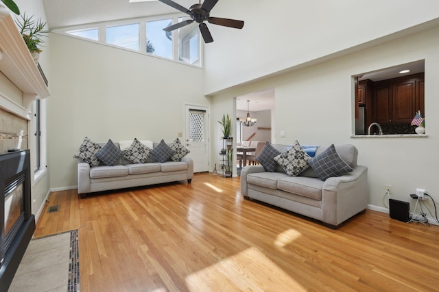 living room featuring visible vents, a towering ceiling, light wood-type flooring, baseboards, and ceiling fan with notable chandelier