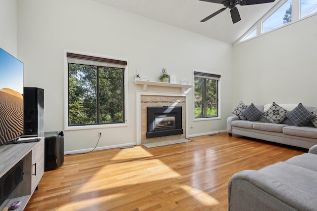 living area with a ceiling fan, high vaulted ceiling, a healthy amount of sunlight, and a tile fireplace