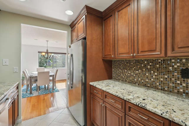 kitchen featuring an inviting chandelier, freestanding refrigerator, backsplash, and light stone countertops