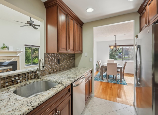 kitchen featuring light tile patterned flooring, light stone countertops, a sink, a glass covered fireplace, and stainless steel appliances