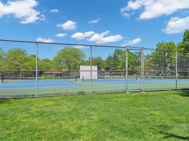 view of tennis court featuring a lawn and fence