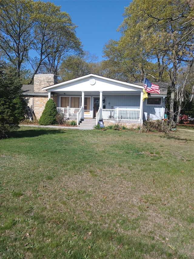 view of front facade with covered porch, a chimney, and a front lawn