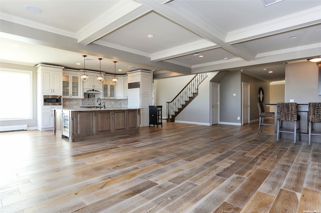 kitchen featuring beam ceiling, light wood-style floors, stainless steel microwave, a large island with sink, and a sink