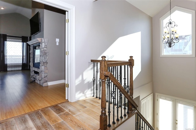 staircase featuring baseboards, a chandelier, a stone fireplace, and wood finished floors