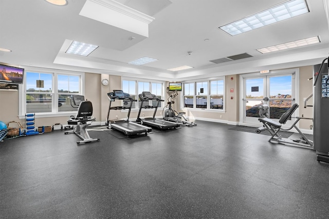 exercise room with a tray ceiling, ornamental molding, and baseboards