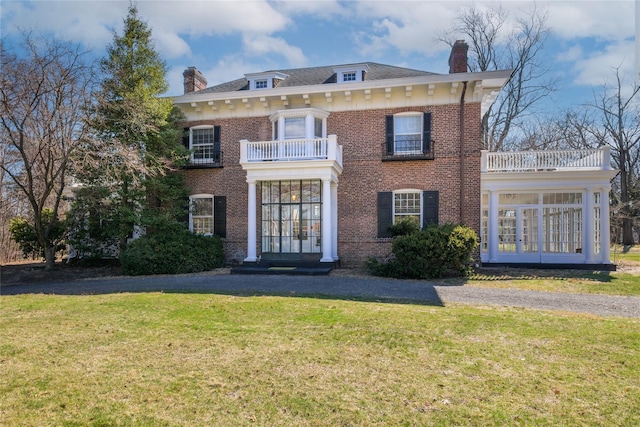 colonial house with french doors, a balcony, a front yard, and a chimney