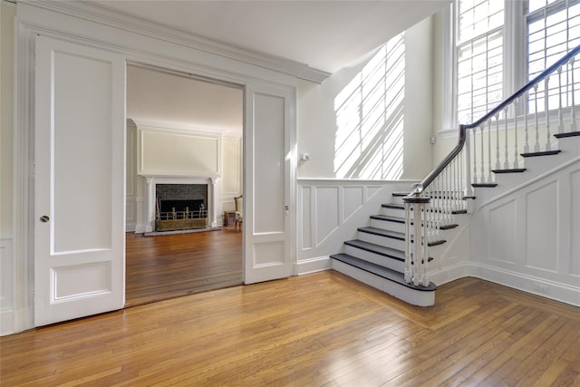 stairs with a fireplace with raised hearth, a decorative wall, hardwood / wood-style flooring, and a wainscoted wall