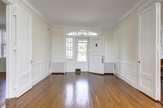 foyer featuring hardwood / wood-style flooring, a wainscoted wall, radiator, ornamental molding, and a decorative wall