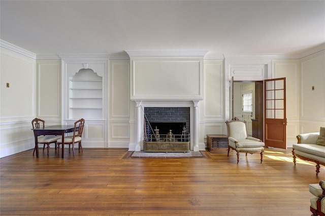 living area with built in features, a decorative wall, and hardwood / wood-style floors