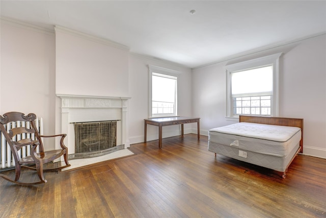 bedroom featuring crown molding, baseboards, a fireplace with flush hearth, and hardwood / wood-style flooring