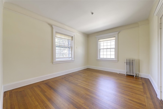 empty room featuring wood-type flooring, baseboards, and radiator heating unit