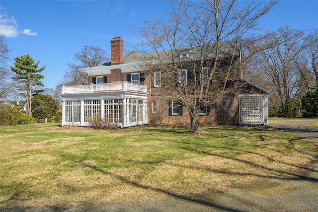 back of property with brick siding, a sunroom, a chimney, a balcony, and a lawn