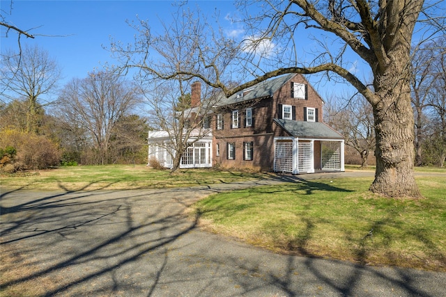 view of front of house featuring a gambrel roof, a chimney, and a front lawn