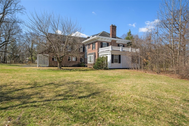 rear view of property featuring a yard, brick siding, a chimney, and a balcony