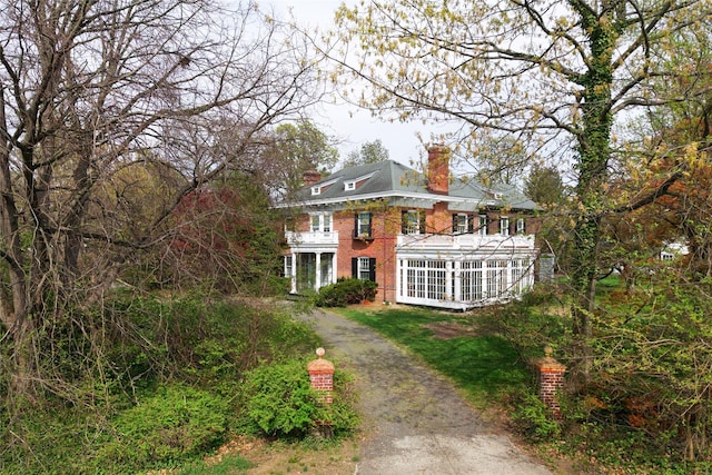 exterior space featuring brick siding, a sunroom, driveway, and a chimney