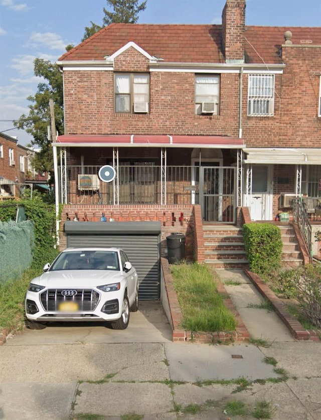 multi unit property featuring a porch, brick siding, cooling unit, and concrete driveway