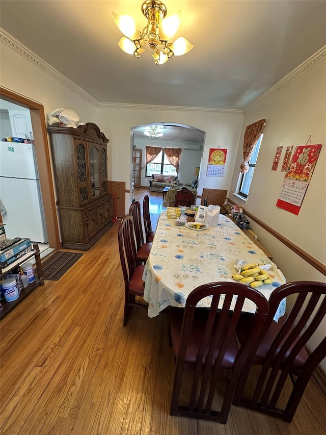 dining room with crown molding, arched walkways, a chandelier, and light wood finished floors