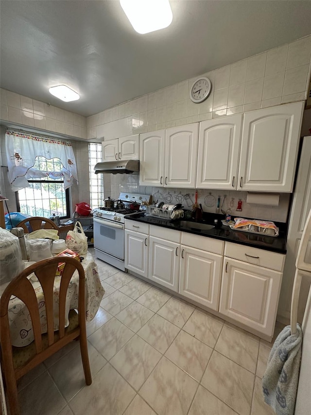 kitchen with dark countertops, gas range gas stove, under cabinet range hood, white cabinets, and tasteful backsplash