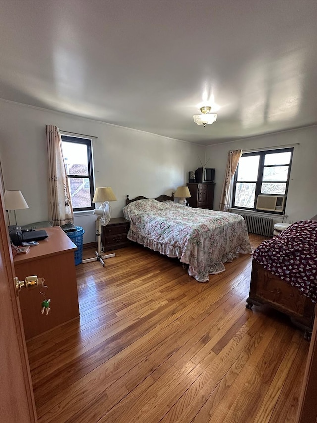 bedroom with light wood-style floors, radiator heating unit, and multiple windows