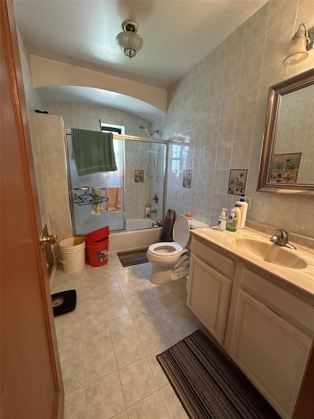 bathroom featuring tile patterned flooring, vanity, toilet, tile walls, and combined bath / shower with glass door
