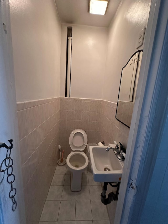 half bath with tile walls, tile patterned flooring, a sink, a wainscoted wall, and toilet