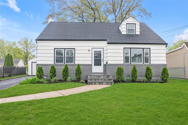 new england style home featuring a front yard, a shingled roof, and fence