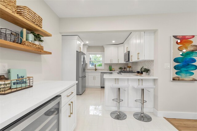 kitchen with beverage cooler, a sink, a kitchen breakfast bar, appliances with stainless steel finishes, and tasteful backsplash