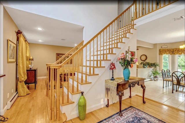 staircase featuring baseboards, a baseboard heating unit, wood finished floors, and visible vents