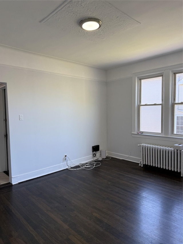 unfurnished room with radiator, baseboards, and dark wood-style flooring