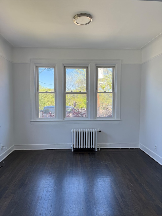 empty room with baseboards, radiator heating unit, dark wood-style floors, and a healthy amount of sunlight