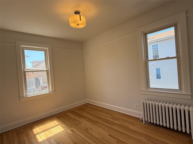 empty room featuring radiator heating unit, baseboards, hardwood / wood-style floors, and a healthy amount of sunlight