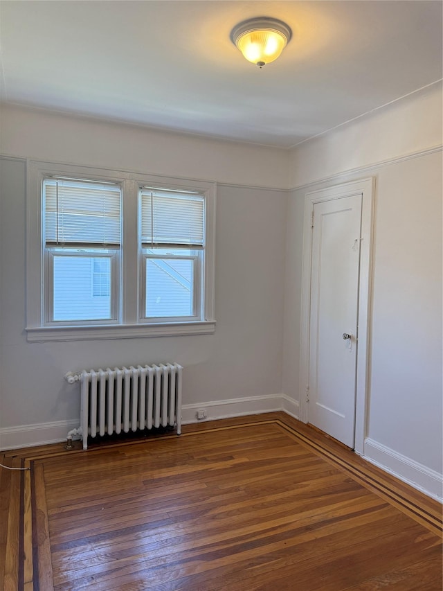 empty room with radiator, baseboards, and wood finished floors