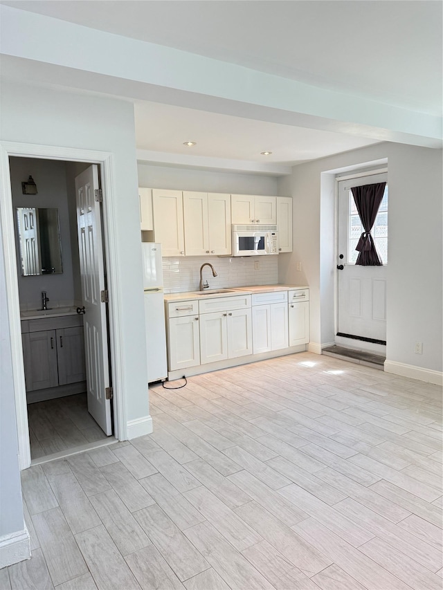 kitchen with a sink, baseboards, white appliances, and light countertops