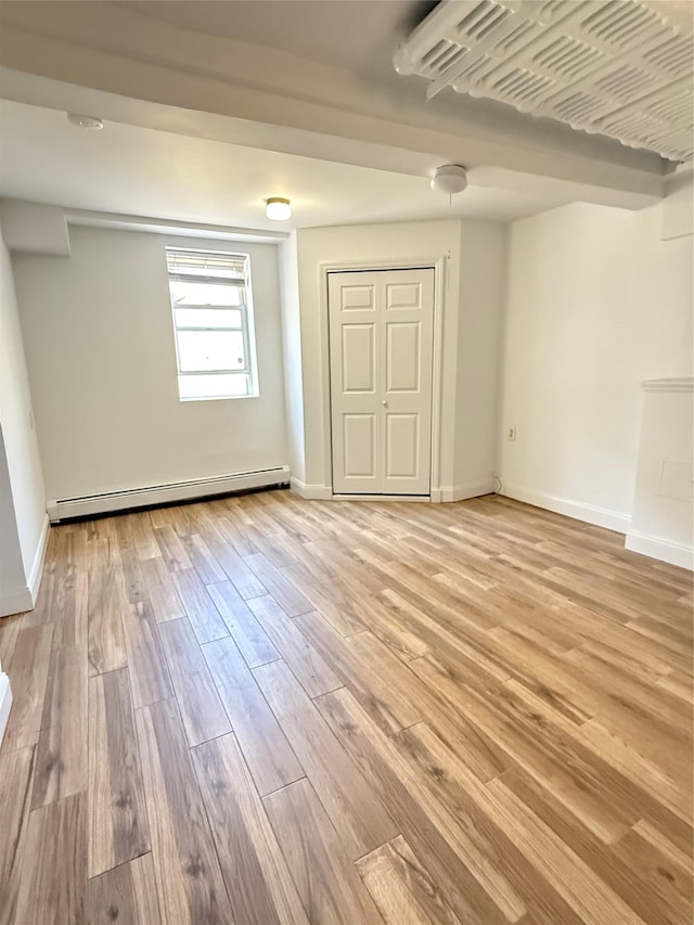 unfurnished bedroom featuring a closet, baseboards, a baseboard heating unit, and light wood-type flooring