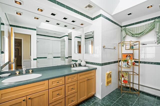 full bathroom with a shower with shower door, tile walls, double vanity, and tile patterned floors