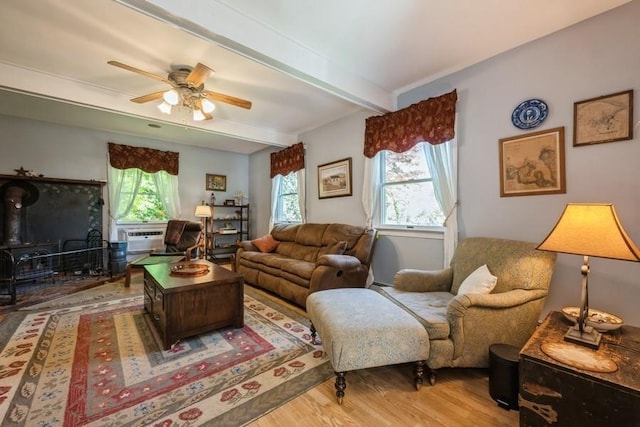 living area featuring beam ceiling, a ceiling fan, a wood stove, and wood finished floors