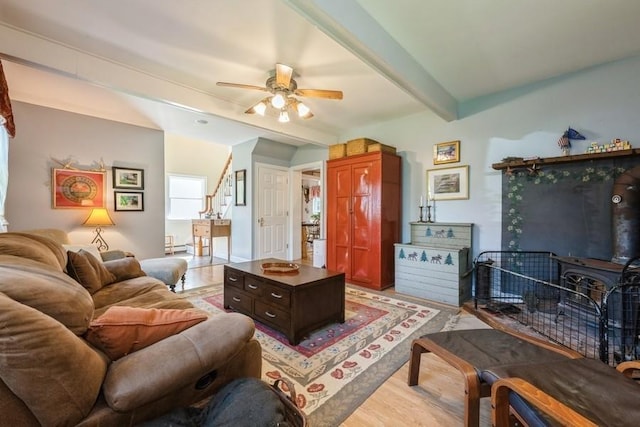 living room with a wood stove, a ceiling fan, light wood-type flooring, beamed ceiling, and stairway
