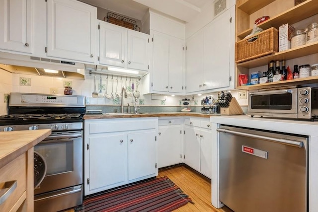 kitchen featuring white cabinetry, under cabinet range hood, a sink, light wood-style flooring, and stainless steel appliances