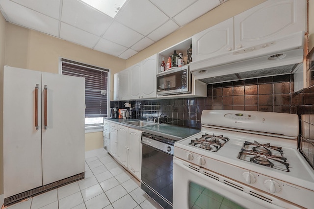 kitchen with white appliances, white cabinetry, under cabinet range hood, a sink, and light tile patterned floors