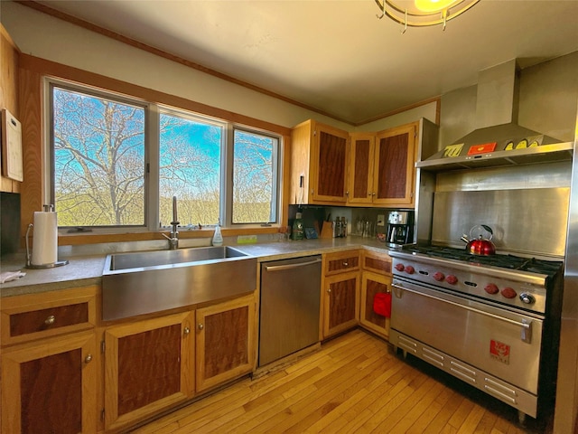 kitchen with brown cabinets, wall chimney range hood, appliances with stainless steel finishes, a sink, and light wood finished floors