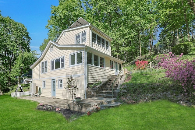 rear view of property featuring stairway, a patio area, and a lawn