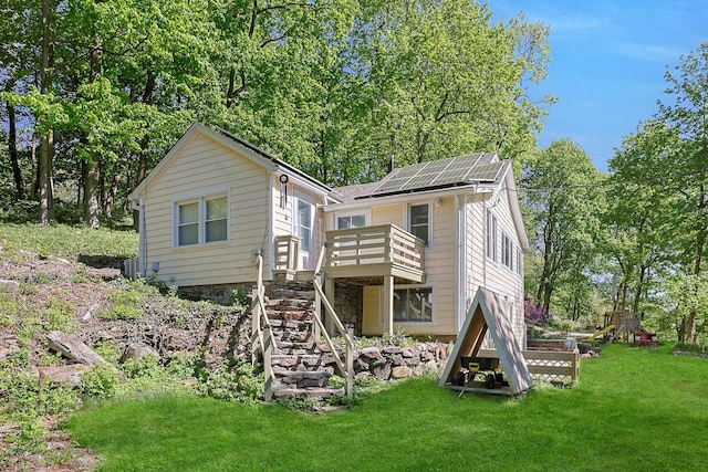 rear view of house with stairway, a deck, a lawn, solar panels, and view of wooded area
