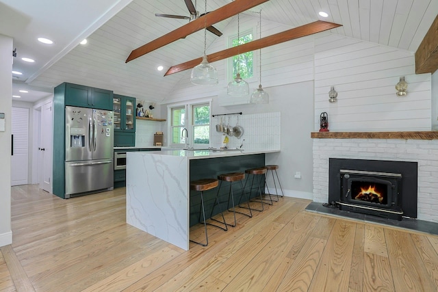 kitchen with appliances with stainless steel finishes, light wood-style floors, a peninsula, a breakfast bar, and a fireplace