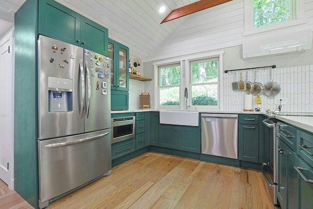 kitchen with appliances with stainless steel finishes, green cabinetry, lofted ceiling, a sink, and light countertops