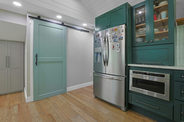 kitchen featuring green cabinets, appliances with stainless steel finishes, a barn door, light wood-style floors, and lofted ceiling