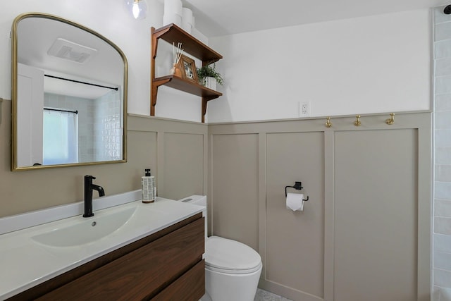 bathroom with a decorative wall, toilet, vanity, wainscoting, and curtained shower