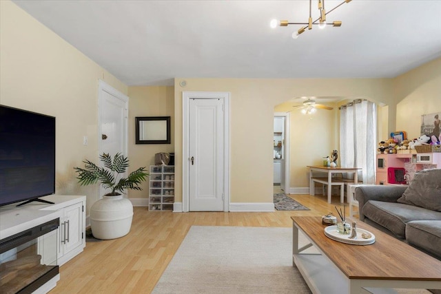 living area featuring baseboards, a notable chandelier, light wood finished floors, and arched walkways