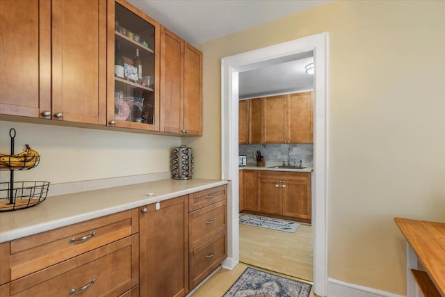 kitchen with a sink, light countertops, brown cabinetry, and glass insert cabinets
